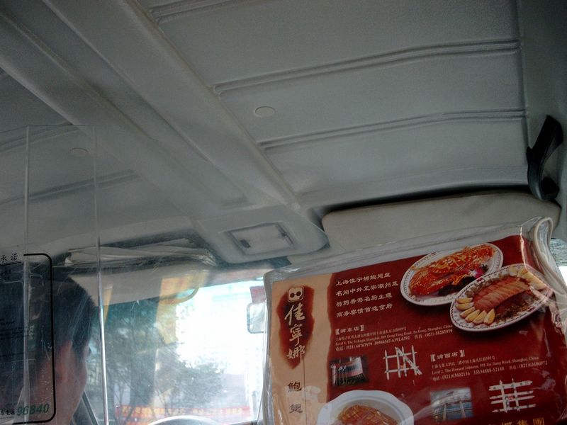 In een taxi
De bestuurder zit achter een plastic scherm, en reclame voor een plaatselijke eettent
